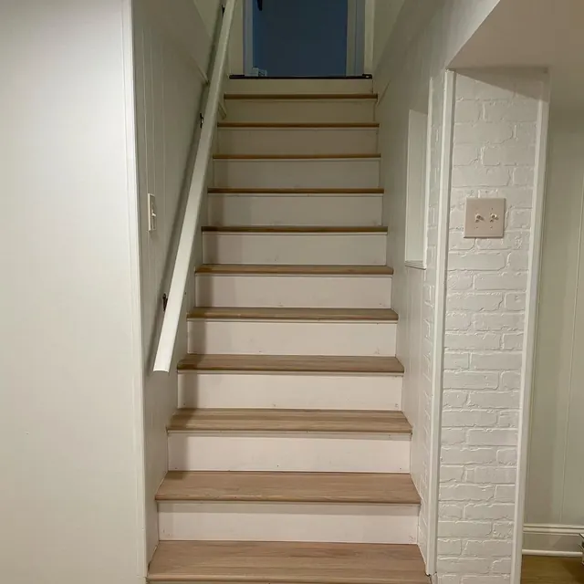 Stairs with light oak treads beside a white painted brick wall
