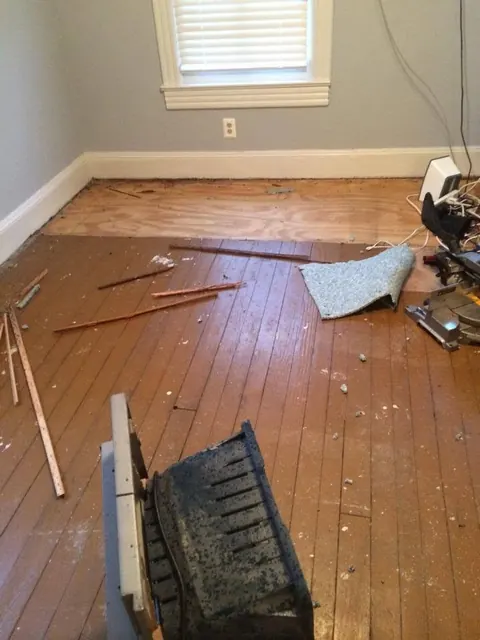 Heart pine floor before restoration, with worn boards, loose trim and a patched subfloor